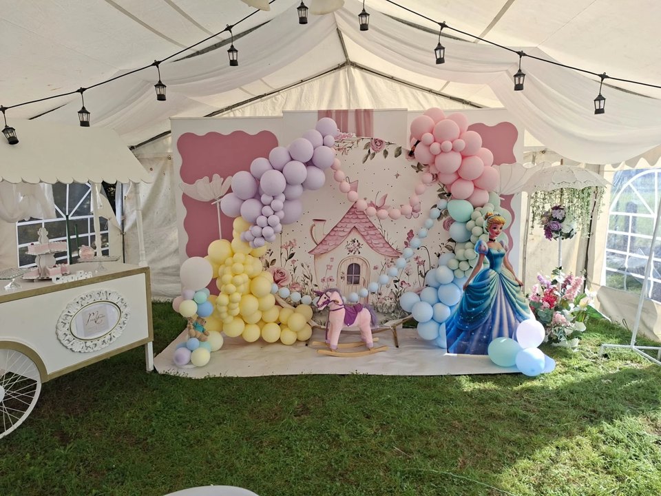 Château de fête et arche de ballons roses, jaunes, bleus et mauves sous une tente